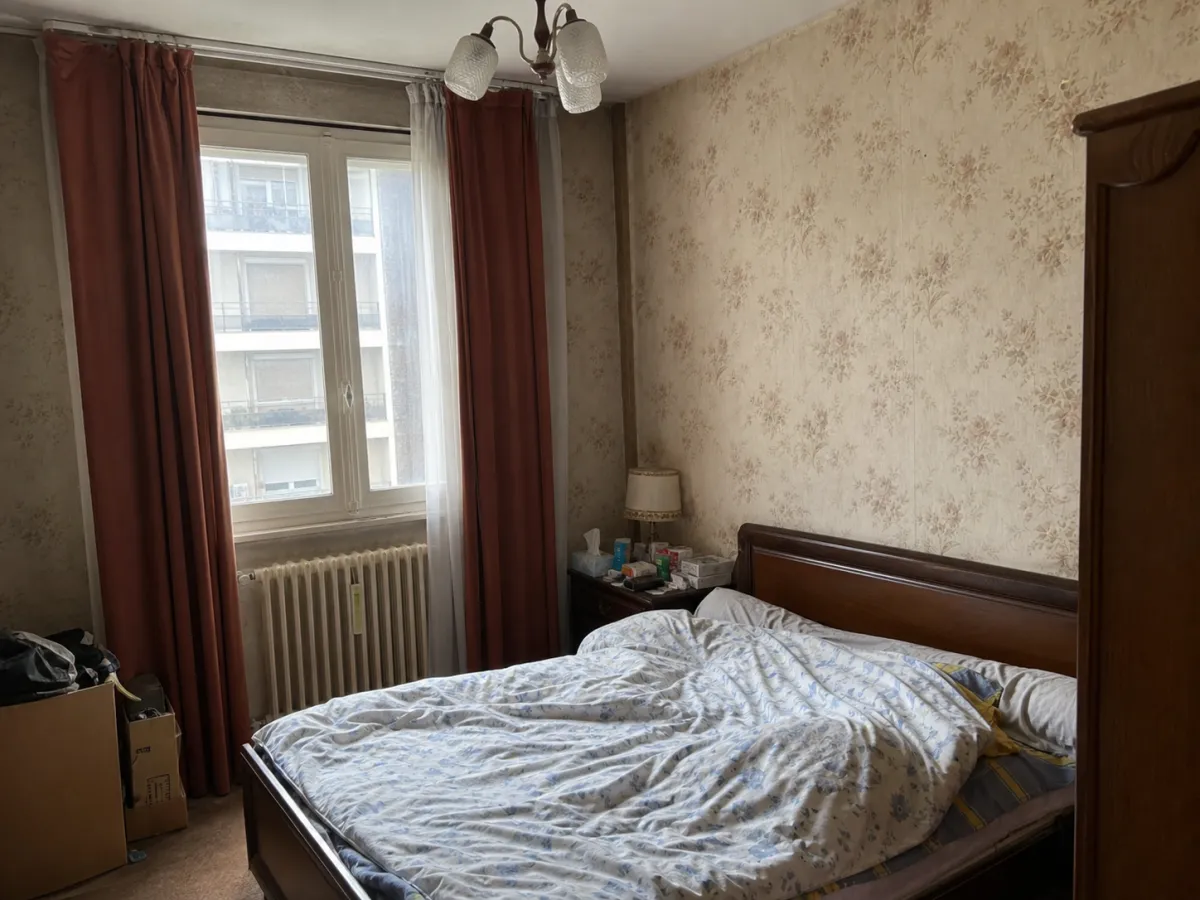 Chambre avant relooking virtuel : lit défait, papier peint défraîchi et rideaux rouges.